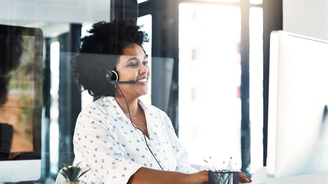 Woman typing on computer with headphones and smiling